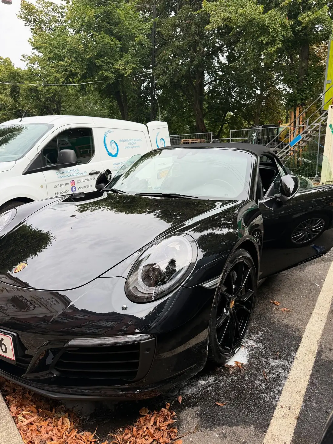 Sort Porsche 911 nyvasket på kundens adresse med Steam Blues servicebil i baggrunden